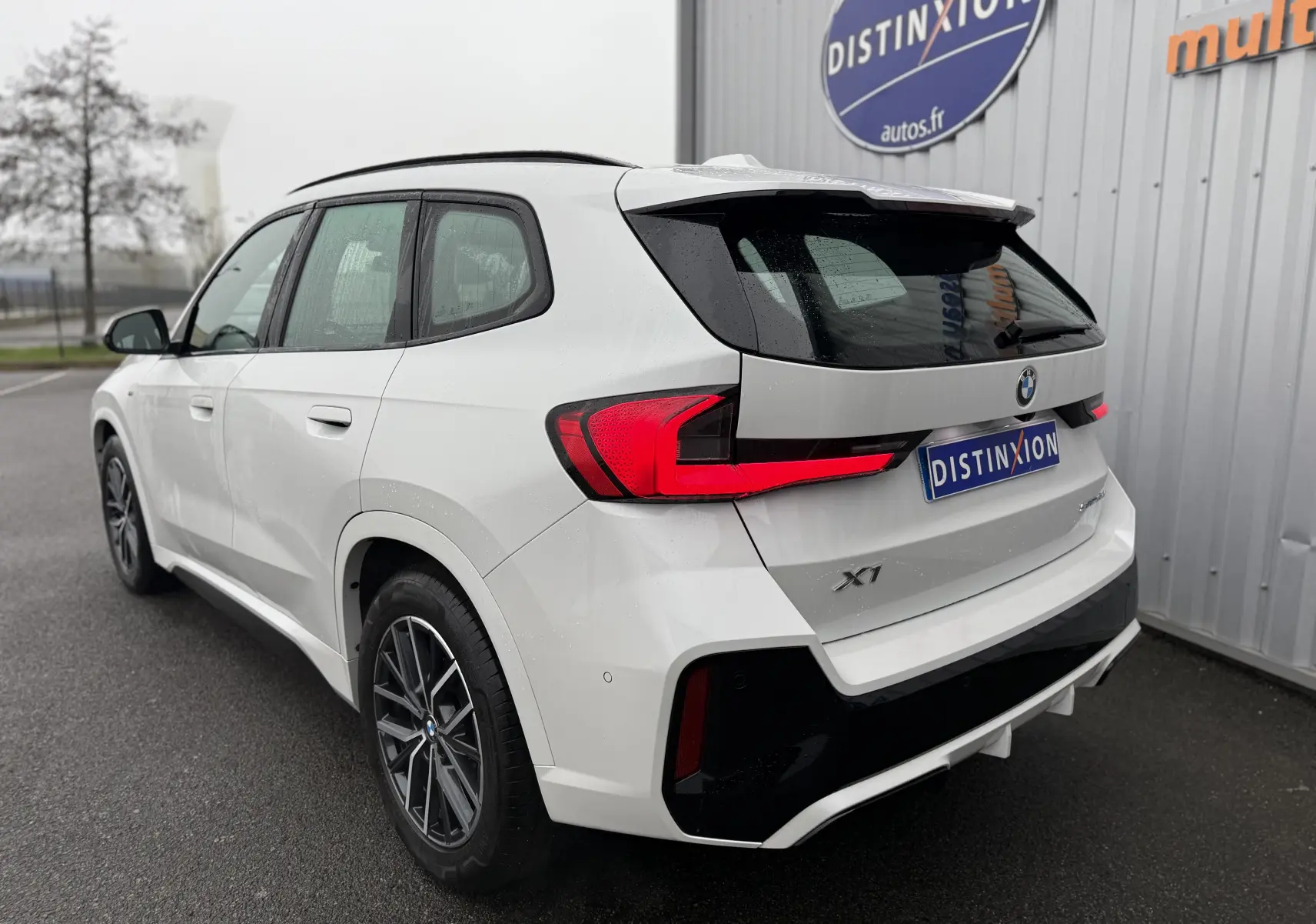 Vue 3/4 arrière droite d'un BMW X1 blanc minéral 2025 avec feux LED et jantes alliage foncé.