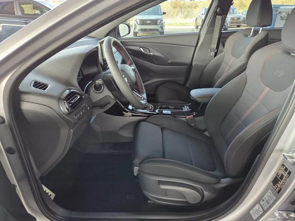 Vue intérieure côté conducteur de la Hyundai i30 SW N-LINE 2025 avec sièges tissu noirs et surpiqûres rouges.