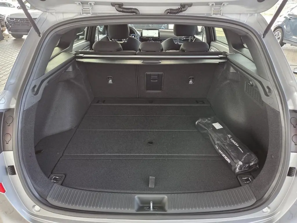 Vue arrière du coffre ouvert d'une Hyundai i30 SW N-LINE gris foncé, montrant un espace de chargement spacieux et un kit Hyundai.