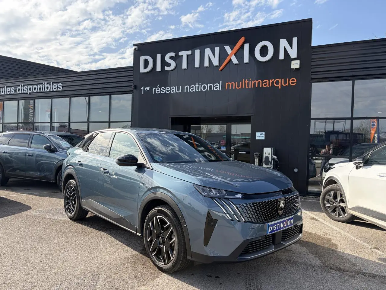 Vue 3/4 avant du Peugeot 3008 bleu Ingaro avec calandre noire et jantes alliage noires devant un showroom Distinxion.
