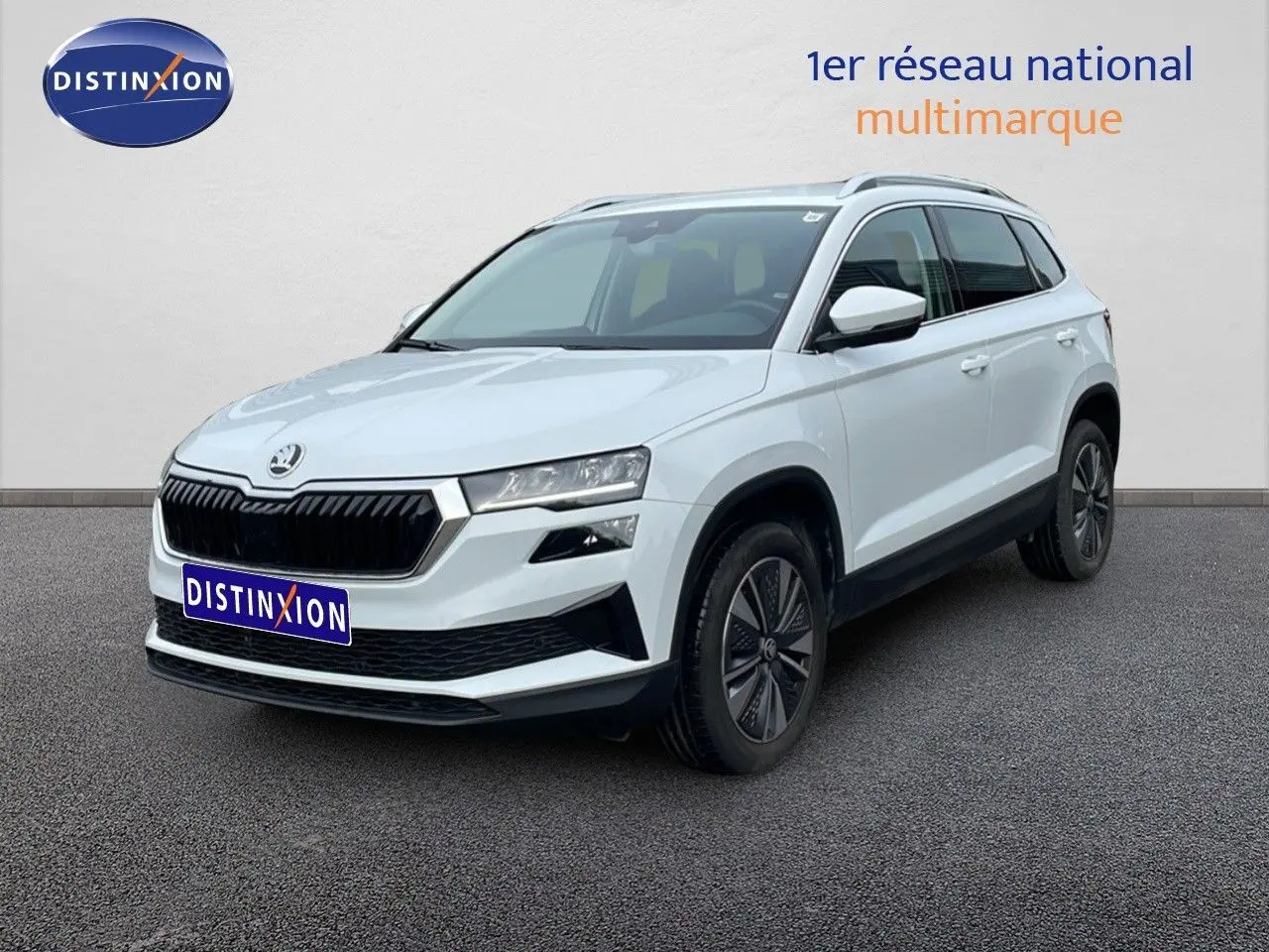 Vue 3/4 avant d'un Skoda Karoq blanc glacier avec calandre noire et jantes alliage foncé sur sol gris.