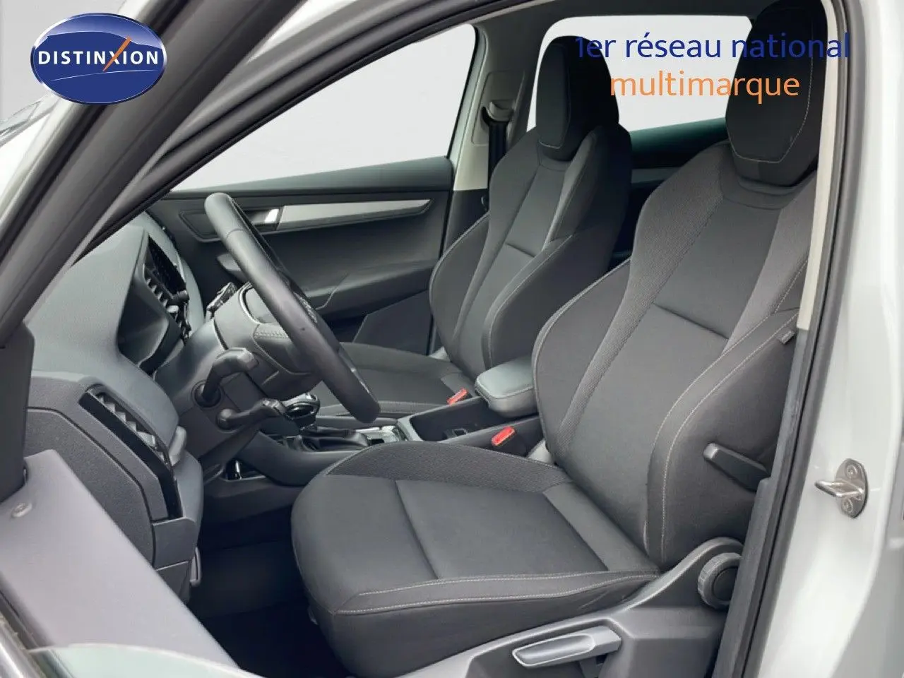 Vue intérieure côté conducteur du Skoda Karoq blanc glacier 2025, sièges tissu noir et volant multifonction.