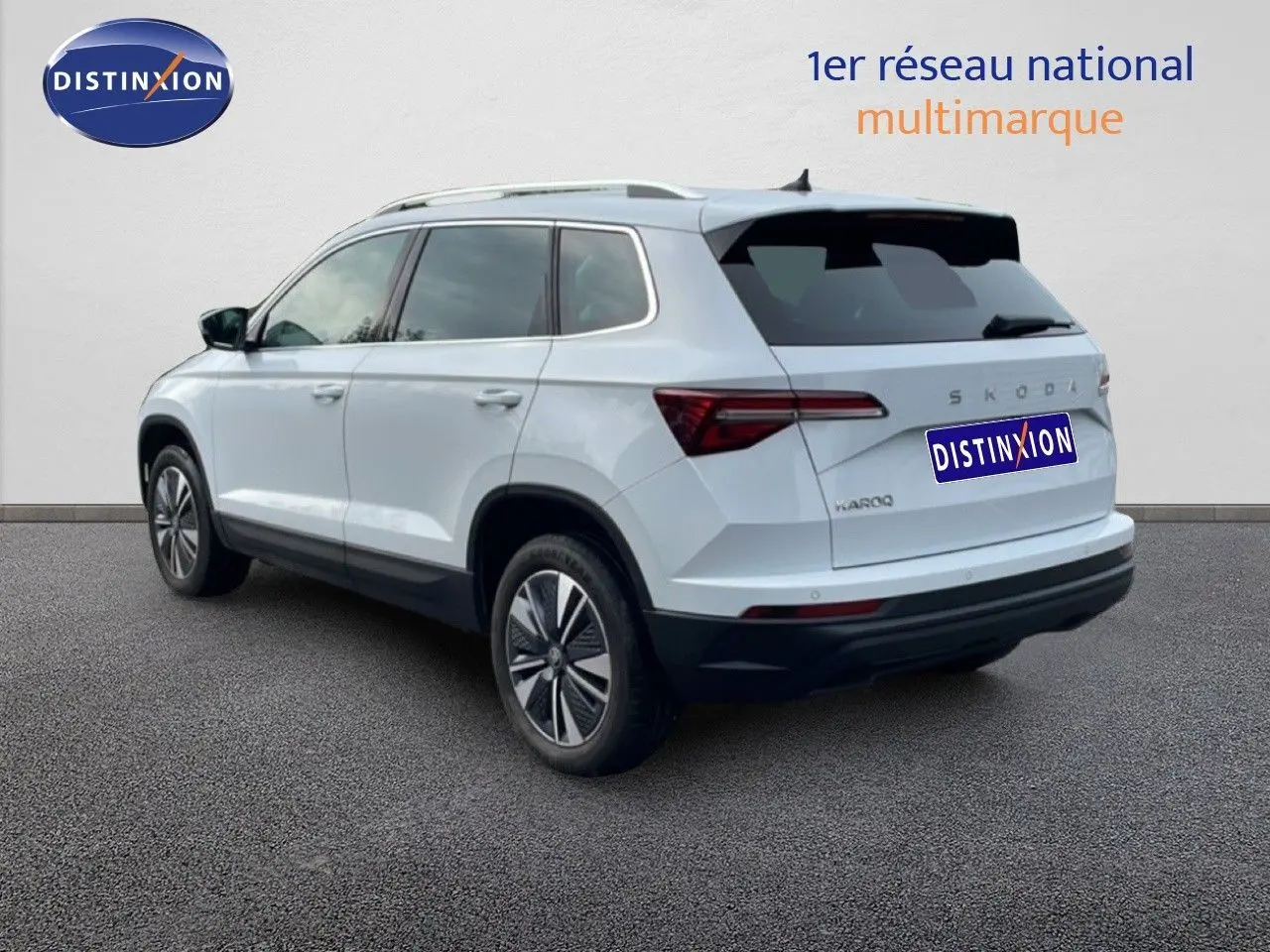 Vue 3/4 arrière droite d’un Skoda Karoq blanc glacier avec jantes alliage et vitres teintées sur fond neutre.