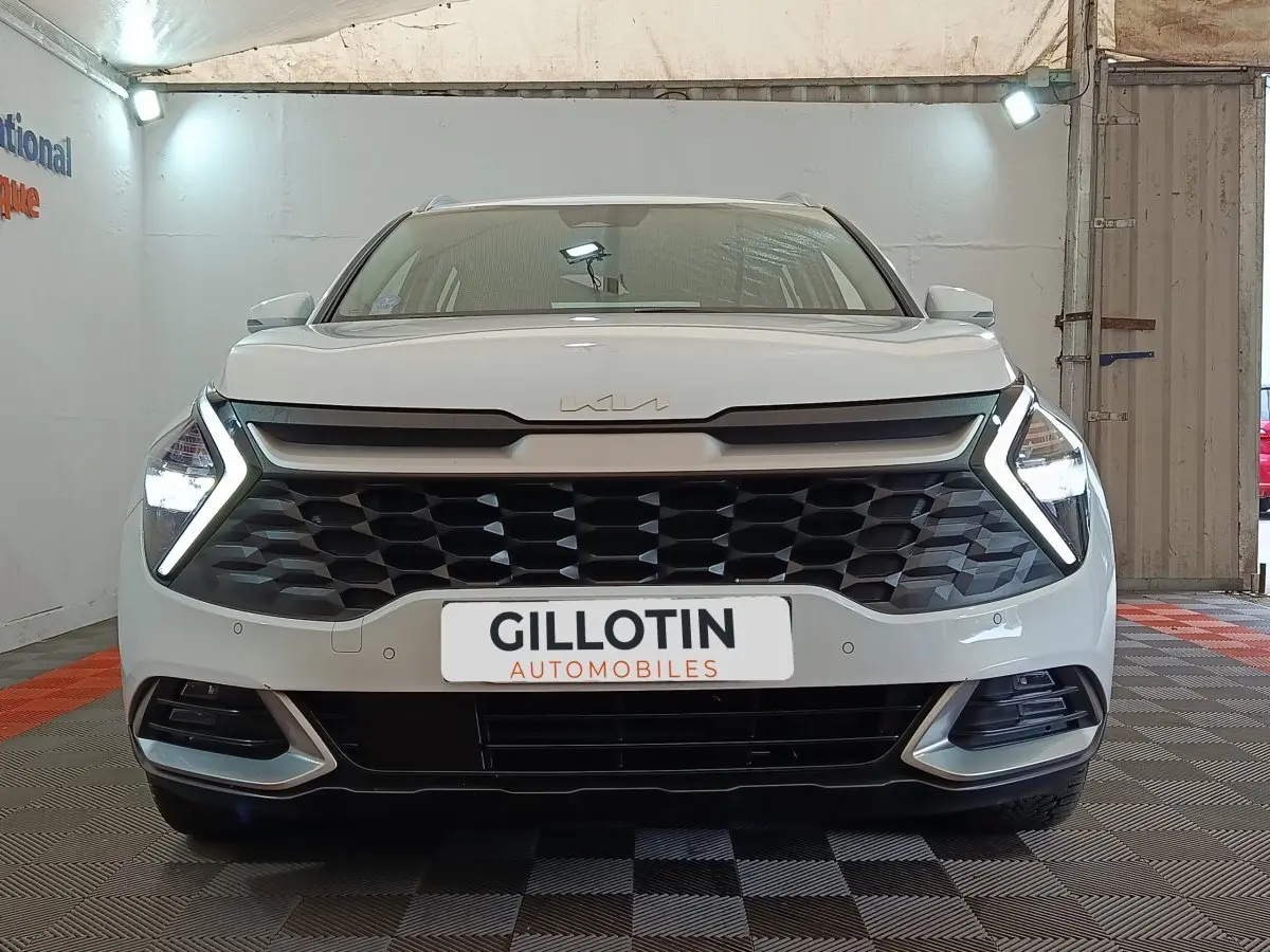 Vue frontale d’un KIA Sportage blanc 2022 avec calandre noire et feux LED en forme de flèche allumés.
