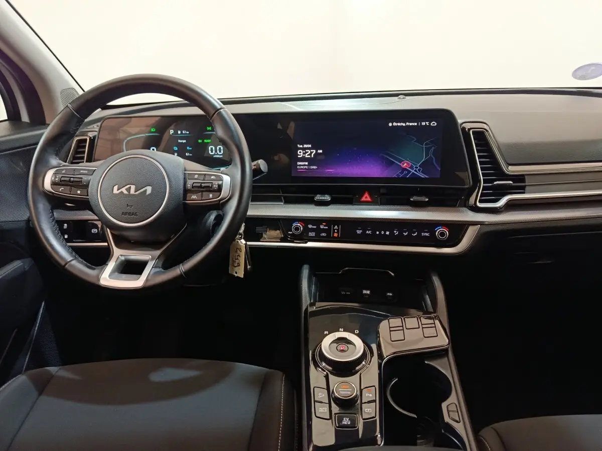 Vue intérieure du tableau de bord et volant du KIA Sportage blanc, avec écran tactile large et commandes modernes.