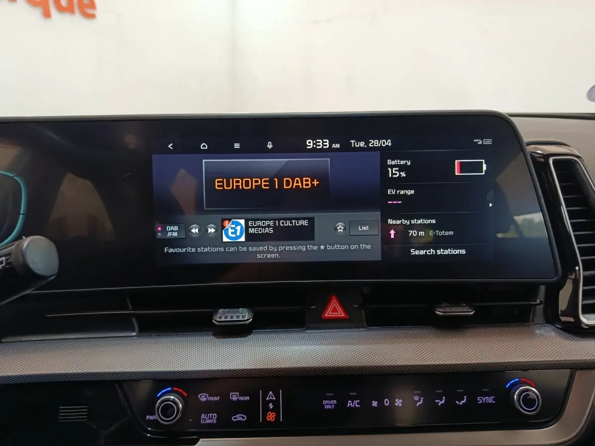 Vue rapprochée du tableau de bord tactile du Kia Sportage blanc 2022, affichant la radio et l'état de la batterie.