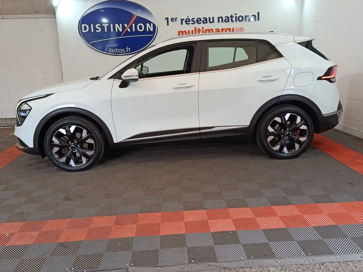 Vue de profil côté gauche d'un KIA SPORTAGE blanc hybride rechargeable avec jantes noires et détails noirs contrastants.