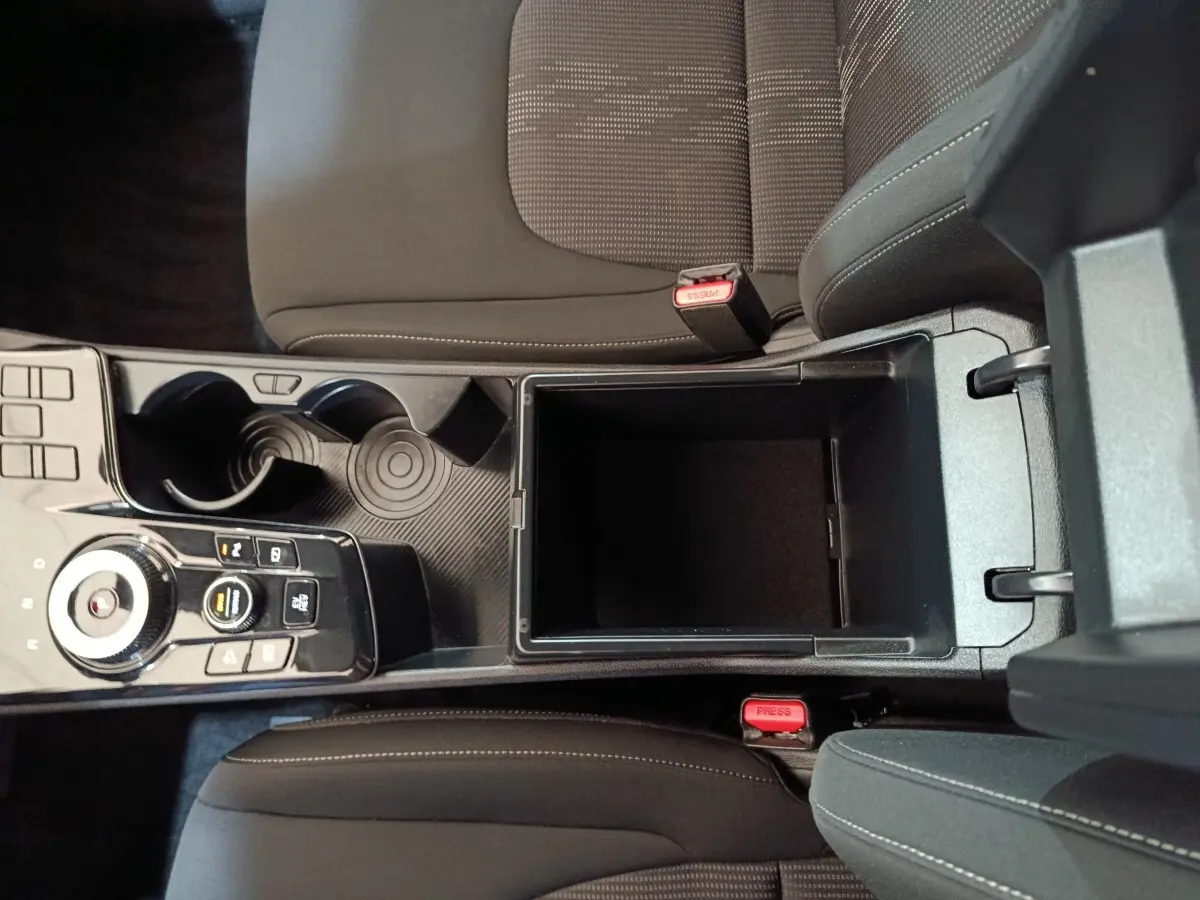 Vue plongeante sur la console centrale noire du Kia Sportage blanc 2022, avec rangement ouvert et commandes de boîte auto.