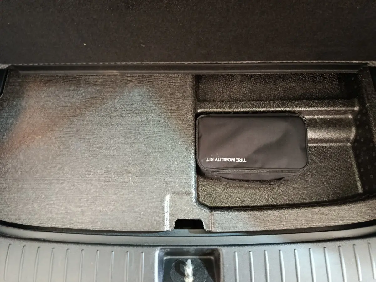 Coffre ouvert du Kia Sportage blanc, vue plongeante sur compartiment avec trousse de mobilité noire.