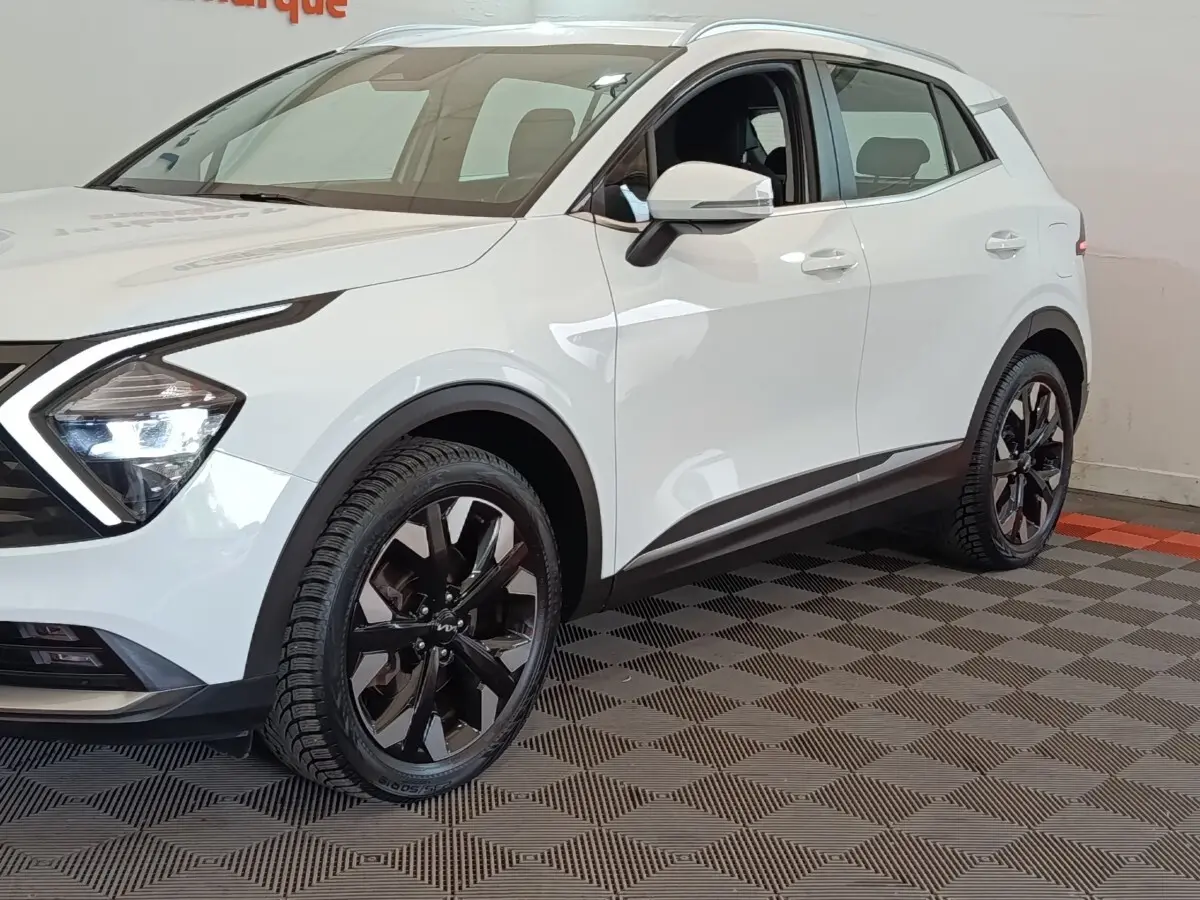 Vue 3/4 avant droit d'un KIA SPORTAGE blanc avec jantes noires et feux LED distinctifs.