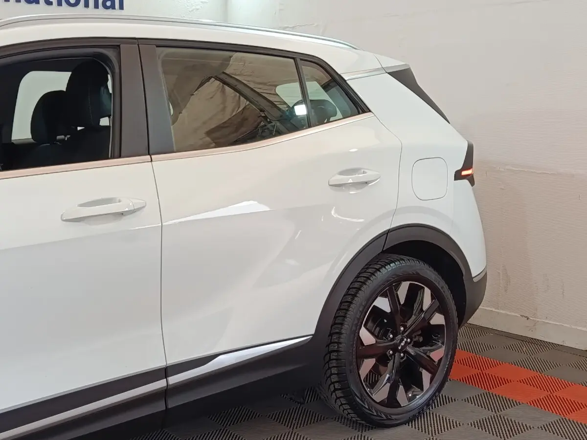 Vue côté droit arrière du Kia Sportage blanc 2022 avec jantes noires et feux arrière LED allumés.