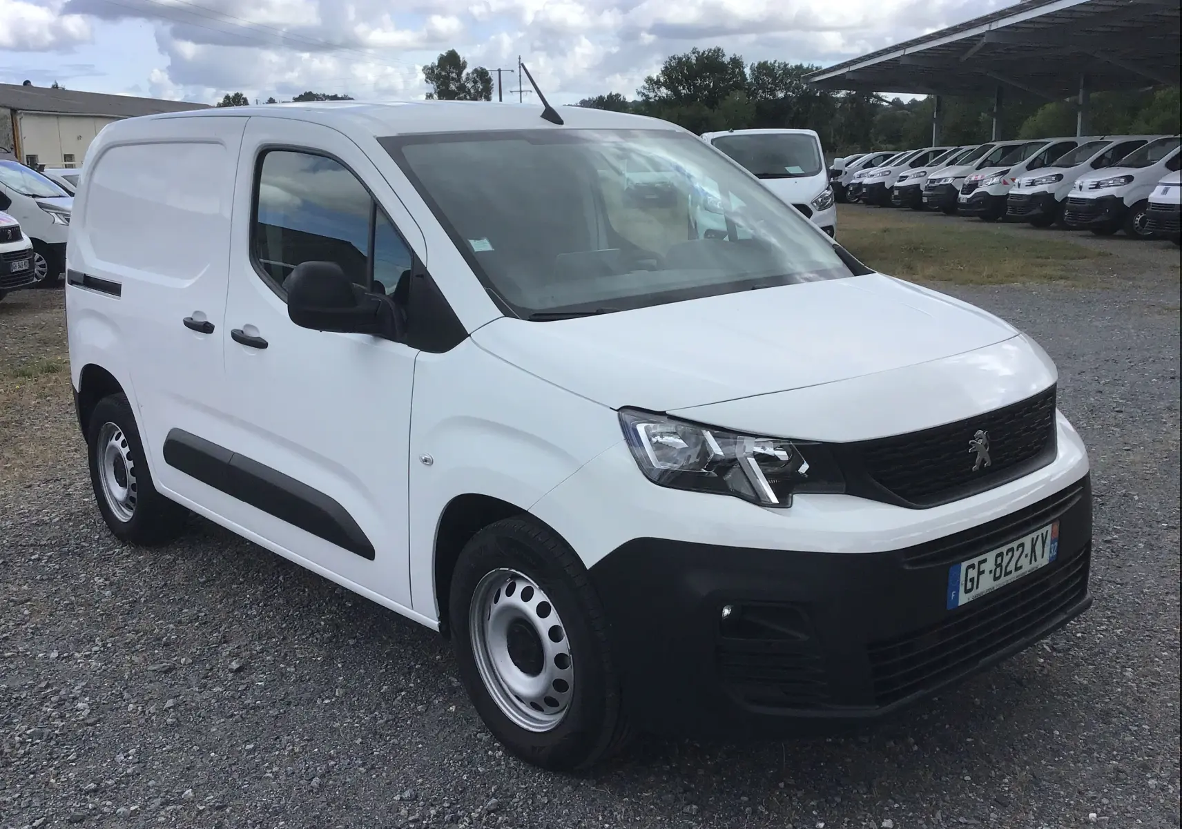 Vue 3/4 avant droite d’un utilitaire Peugeot Partner blanc 2022 avec protections noires et plaque de protection sous moteur visible.
