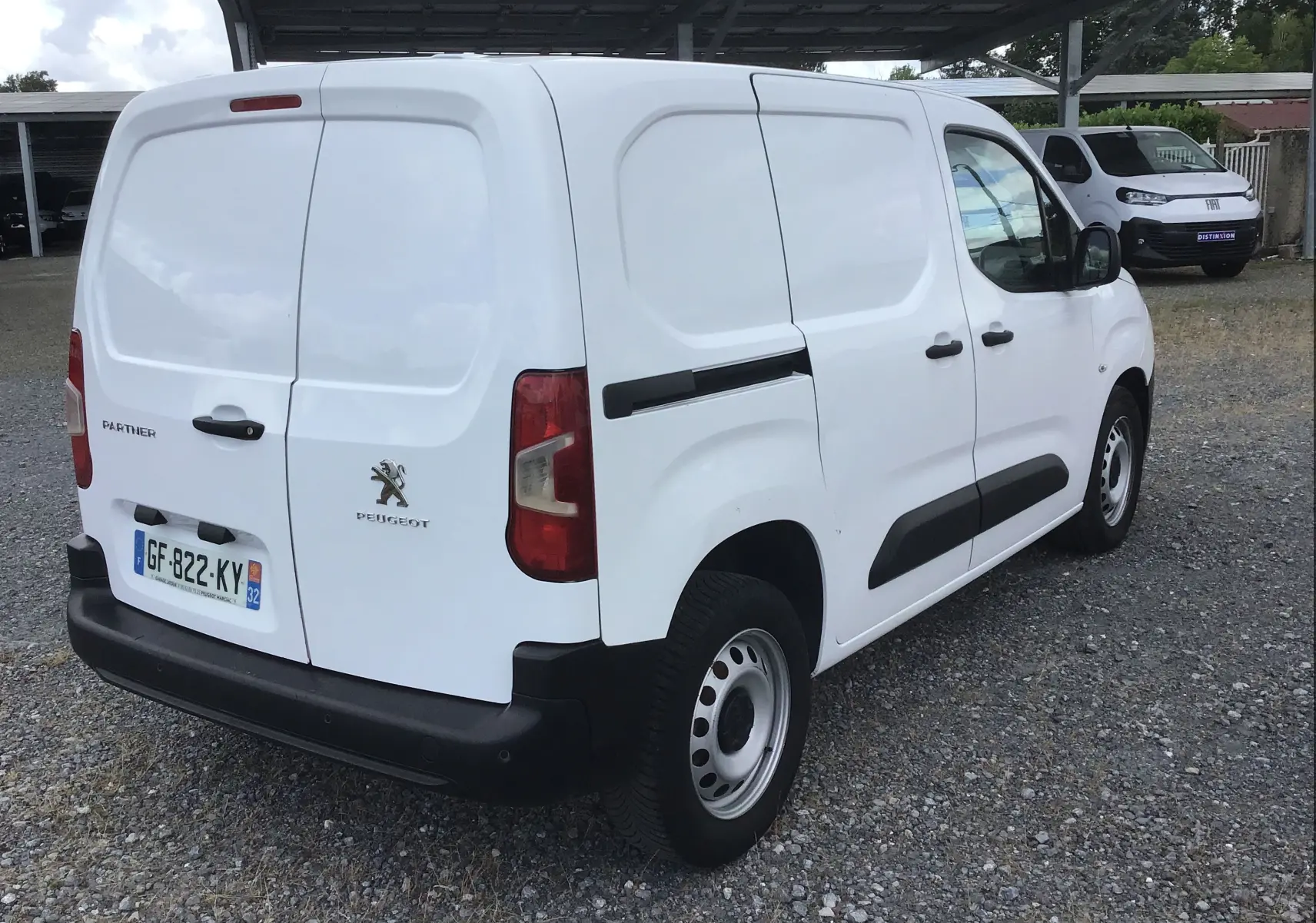 Vue 3/4 arrière droite d’un Peugeot Partner blanc utilitaire avec portes arrière battantes et protections noires.