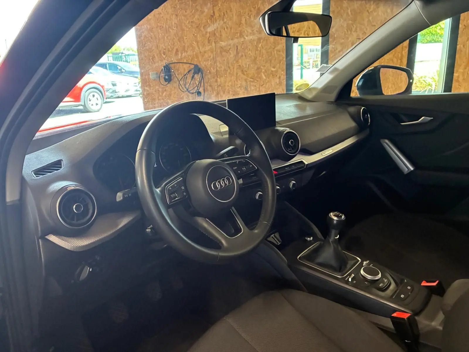 Intérieur noir de l'Audi Q2 30 1.6 TDI 2020 vu côté conducteur, volant multifonction et boîte manuelle visibles.