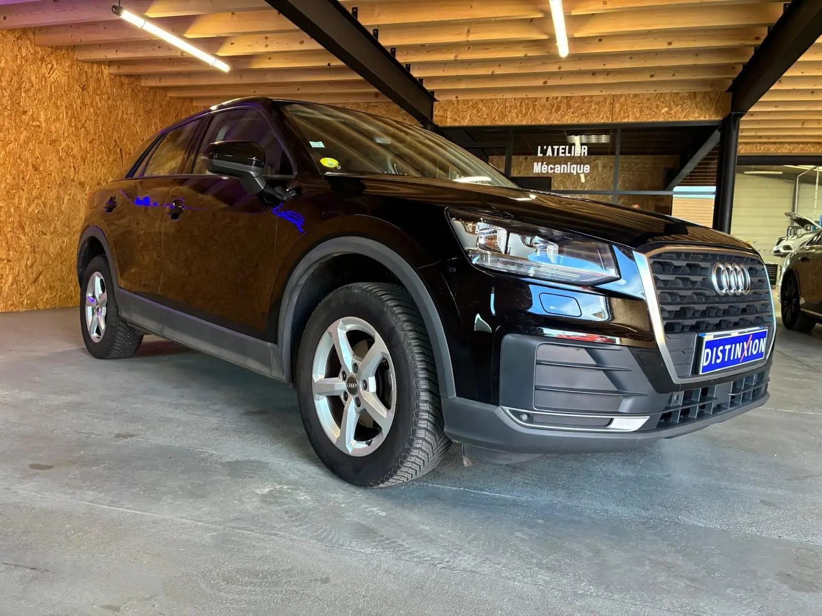 Audi Q2 noir vue 3/4 avant droit dans un garage, mettant en valeur sa calandre distinctive et ses jantes argentées.