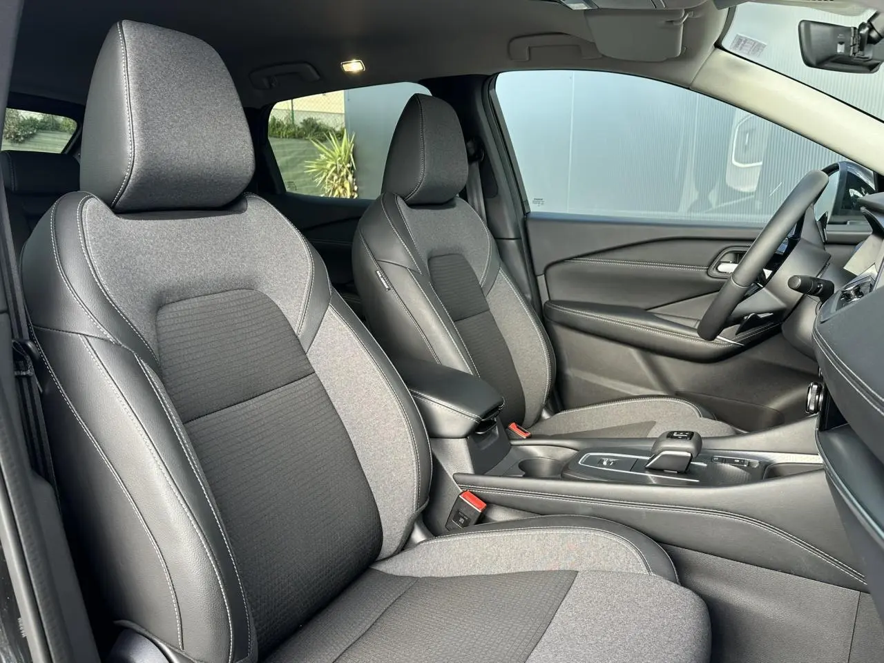 Vue intérieure côté droit des sièges avant gris et noir du Nissan Qashqai 2025 avec console centrale et volant cuir.