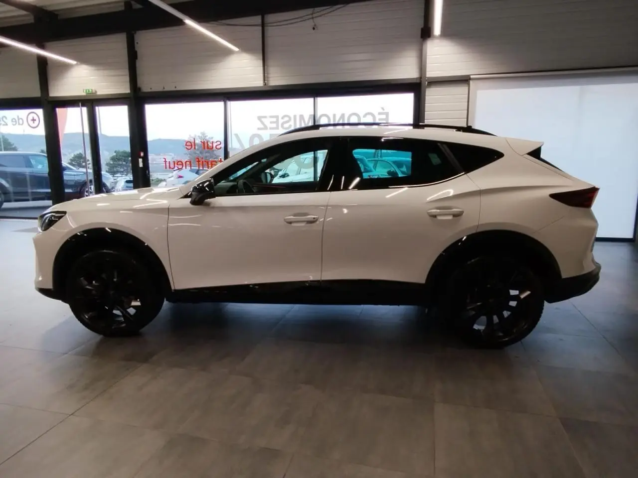 Vue de profil côté gauche d'un CUPRA Formentor blanc Nevada avec jantes noires en intérieur showroom.