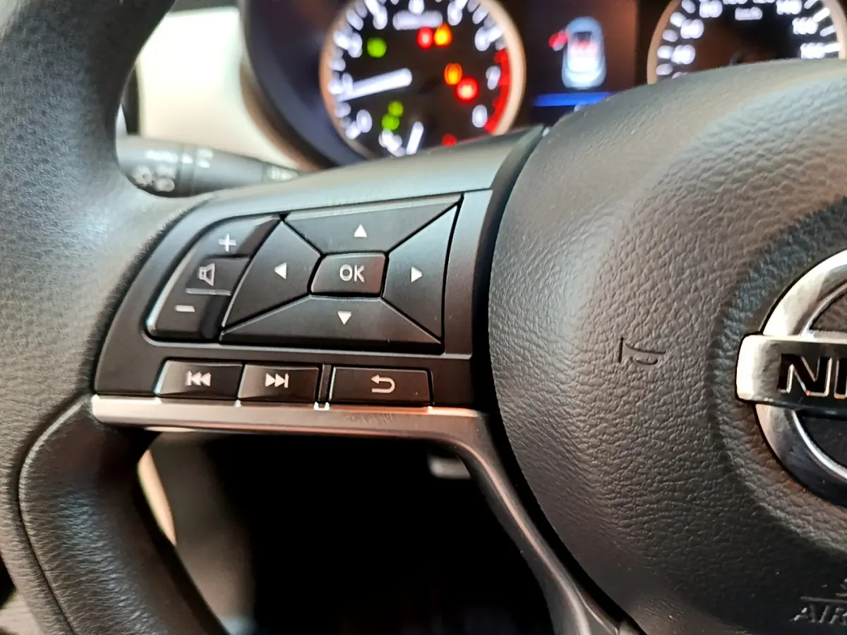 Gros plan sur le volant noir de la Nissan Micra IG-T 92 Acenta 2022 avec commandes multifonctions et tableau de bord lumineux.