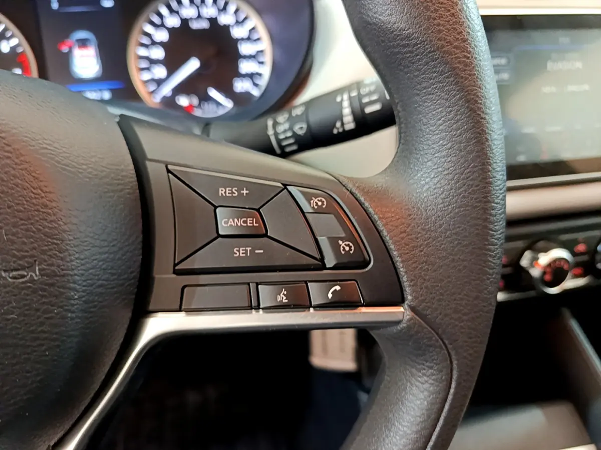 Gros plan sur le volant noir de la Nissan Micra IG-T 92 Acenta 2022, avec commandes de régulateur de vitesse et téléphone.