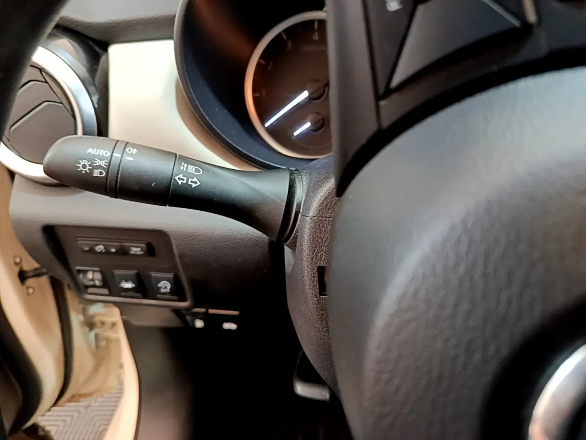 Gros plan sur la manette de clignotants et le tableau de bord noir du Nissan Micra blanc, côté gauche du volant.