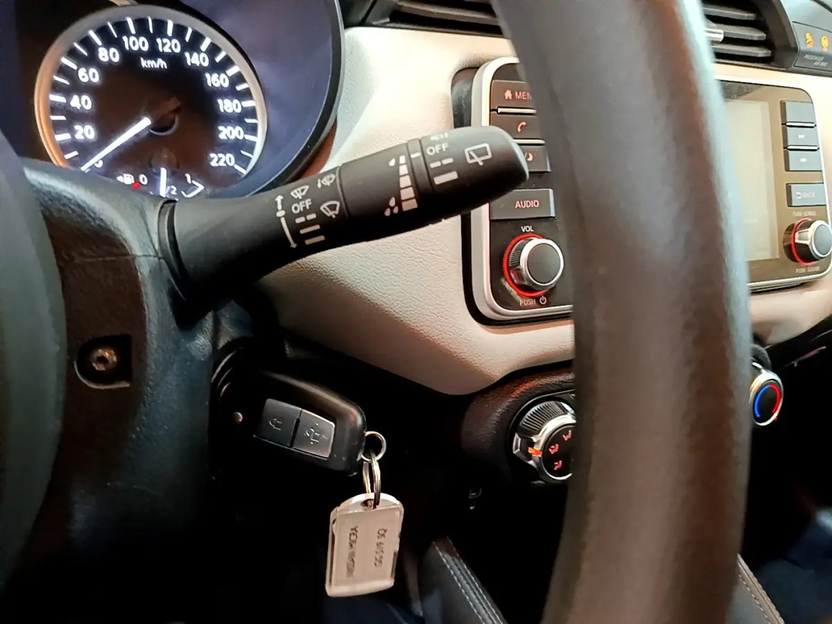 Vue rapprochée du tableau de bord et du volant d'une Nissan Micra blanche, avec clé insérée et commandes visibles.