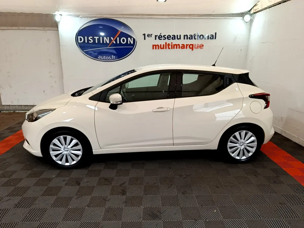 Profil côté gauche d'une Nissan Micra IG-T 92 Acenta blanche 2022, en intérieur sur sol damier noir et orange.