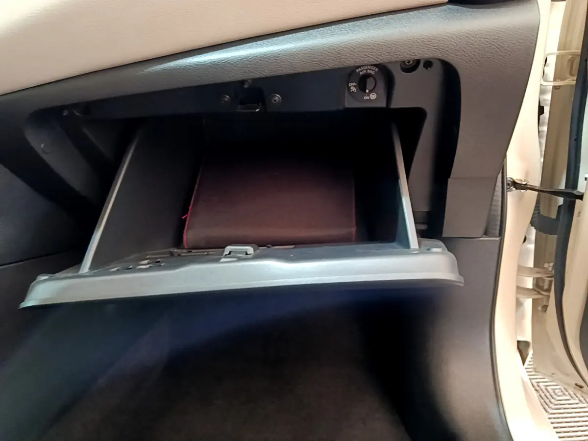 Gant de boîte à gants ouvert côté passager d'une Nissan Micra blanche, montrant l'intérieur noir et un manuel.