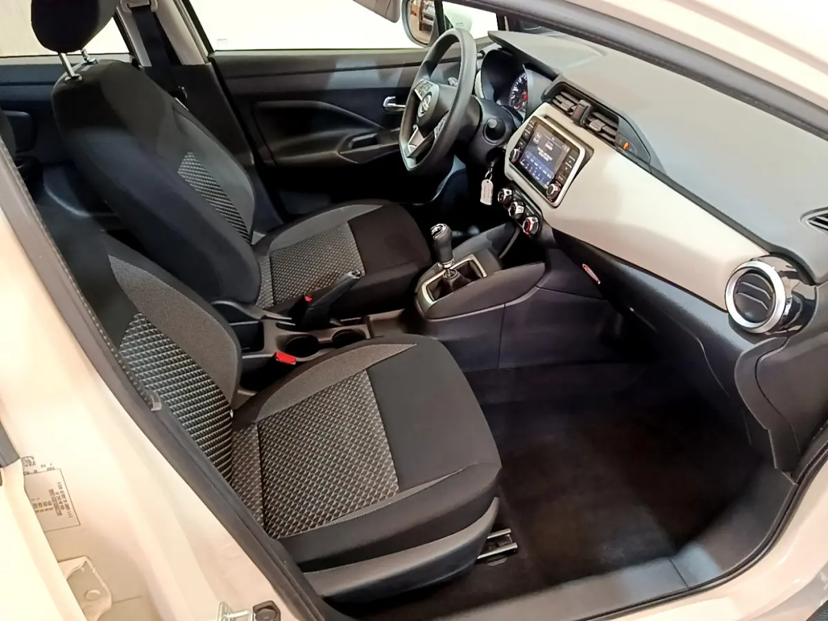 Vue intérieure côté conducteur de la Nissan Micra blanche 2022, montrant tableau de bord et sièges noirs à motifs.