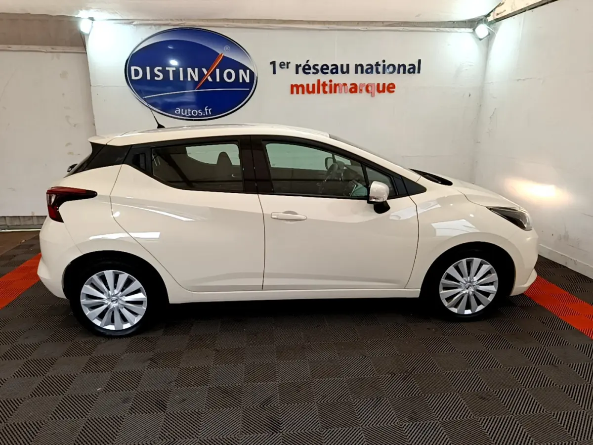 Profil droit d'une Nissan Micra IG-T 92 Acenta blanche 2022, dans un showroom avec sol noir et rouge.