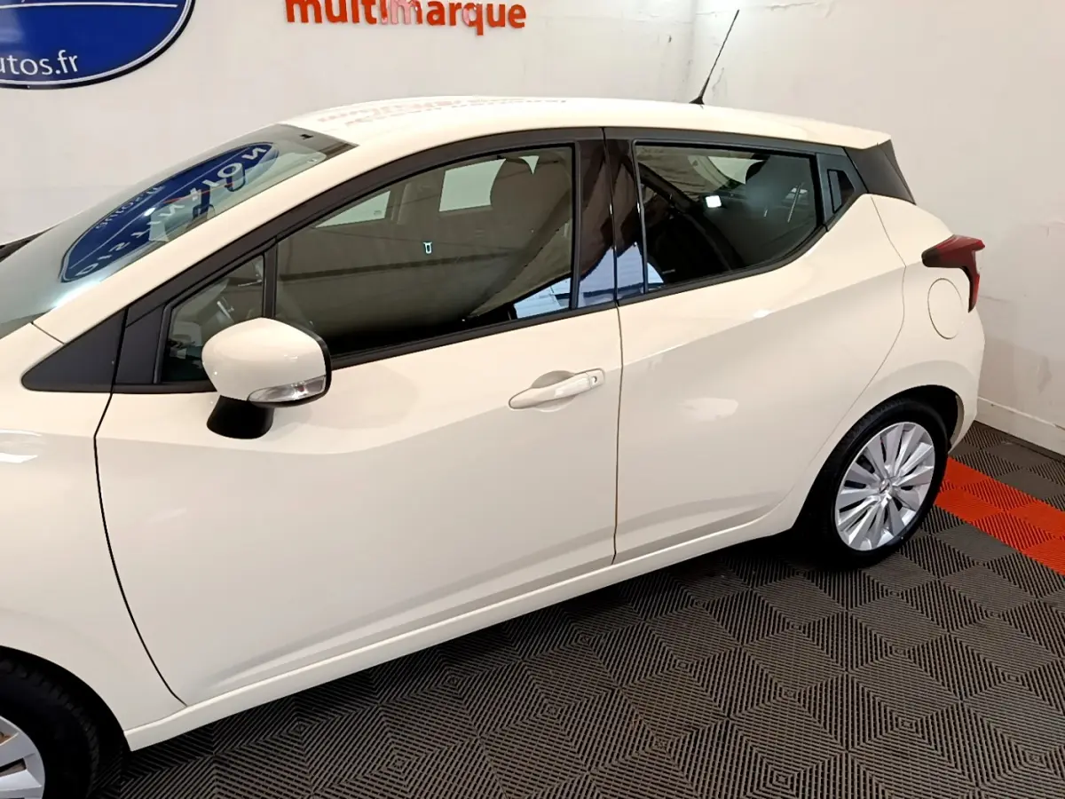 Profil côté gauche d'une Nissan Micra blanche 2022 avec rétroviseur et poignées assortis, sur sol à damier noir et rouge.