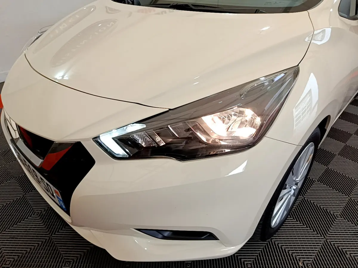 Vue 3/4 avant droit d'une Nissan Micra IG-T 92 Acenta blanche avec phares LED allumés et jantes alliage visibles.