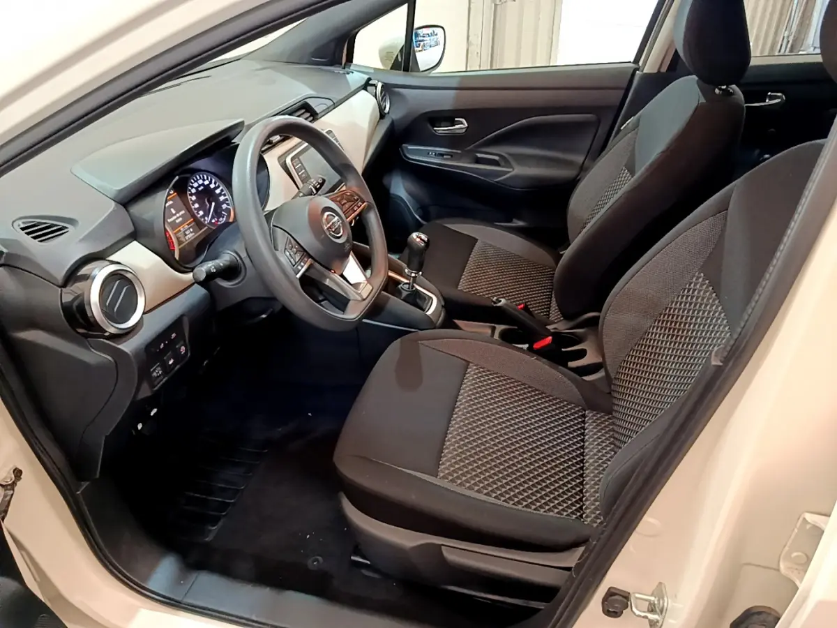 Intérieur avant côté conducteur d'une Nissan Micra blanche 2022 avec sièges tissu noirs et volant multifonctions.