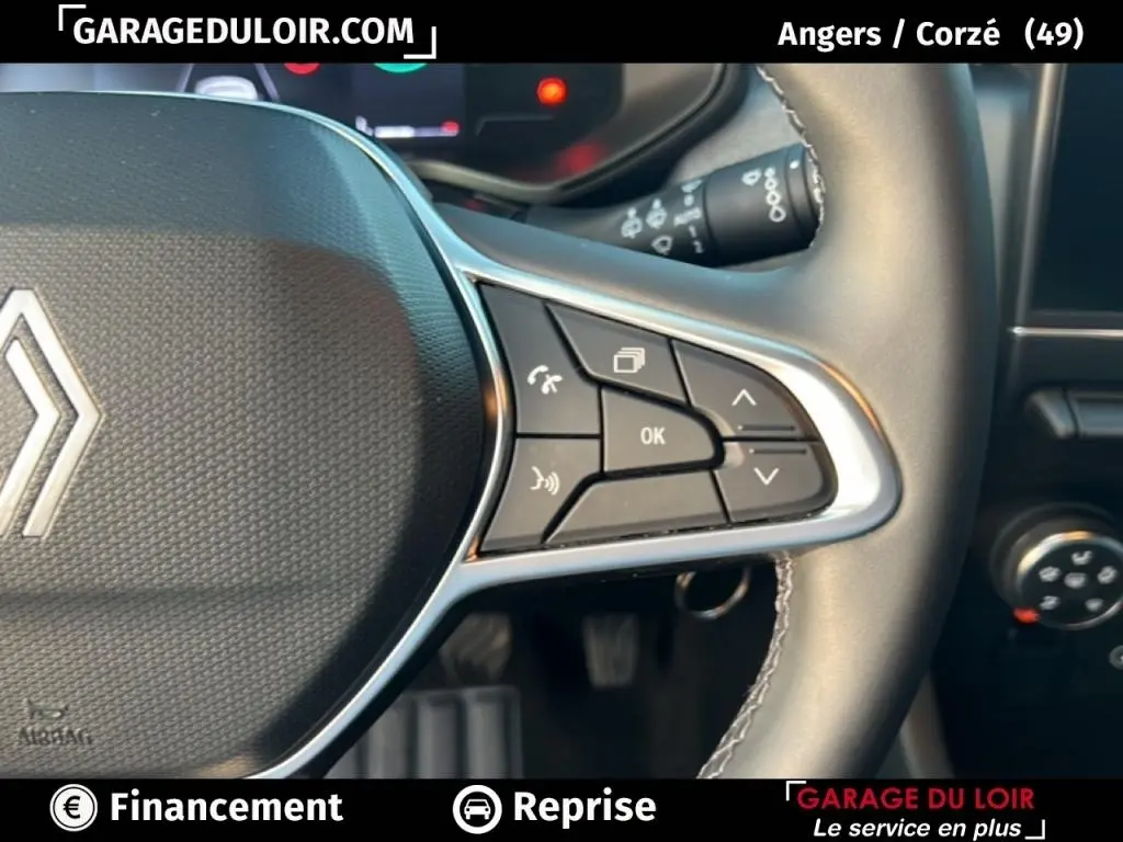 Gros plan sur le volant cuir synthétique noir de la Renault Clio 2025, avec commandes multifonctions et logo central visible.