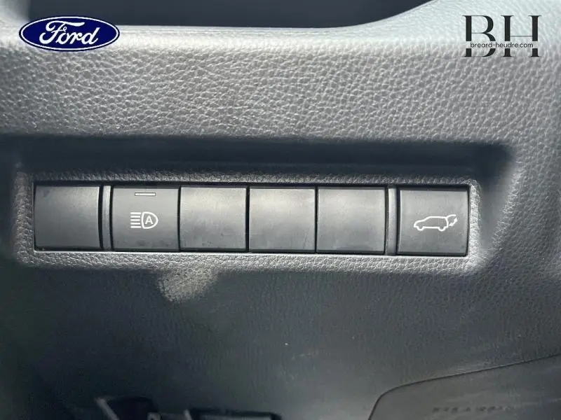 Boutons de commande intérieurs noirs sur tableau de bord, avec symbole d'ouverture de coffre et gestion des phares, Toyota RAV4 noir métallisé.