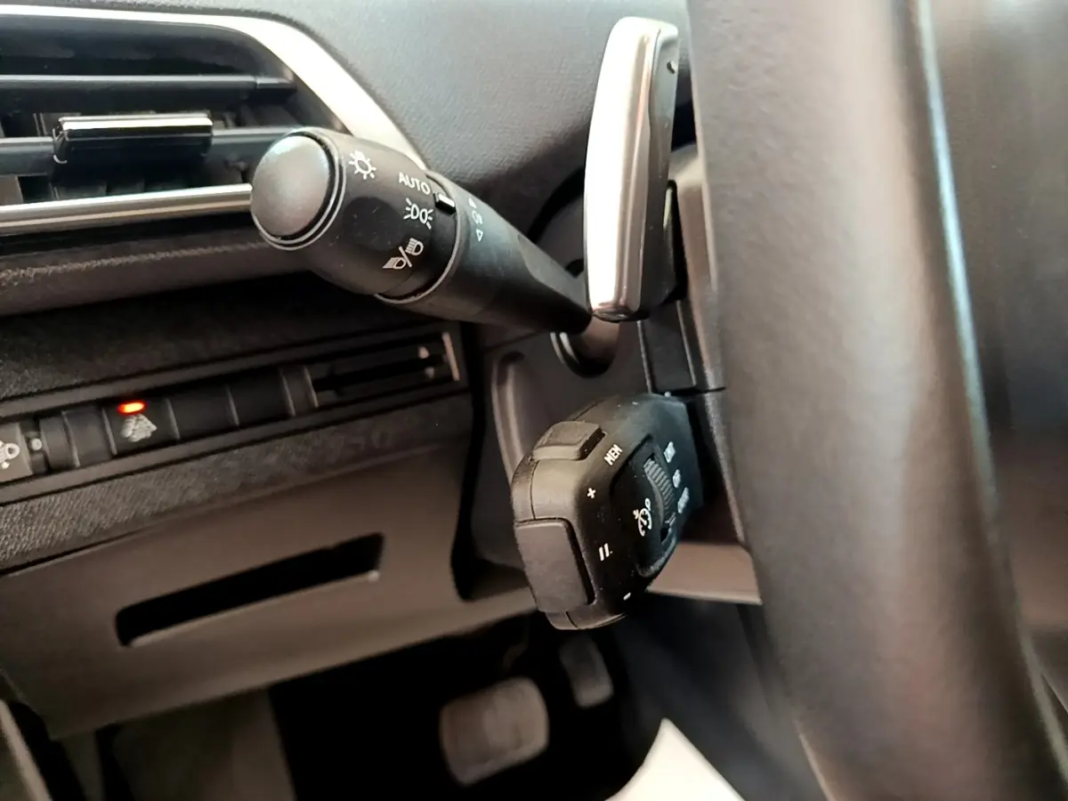 Gros plan sur la commande multifonction noire et le commodo d’éclairage à gauche du volant noir du Peugeot 3008 bleu.