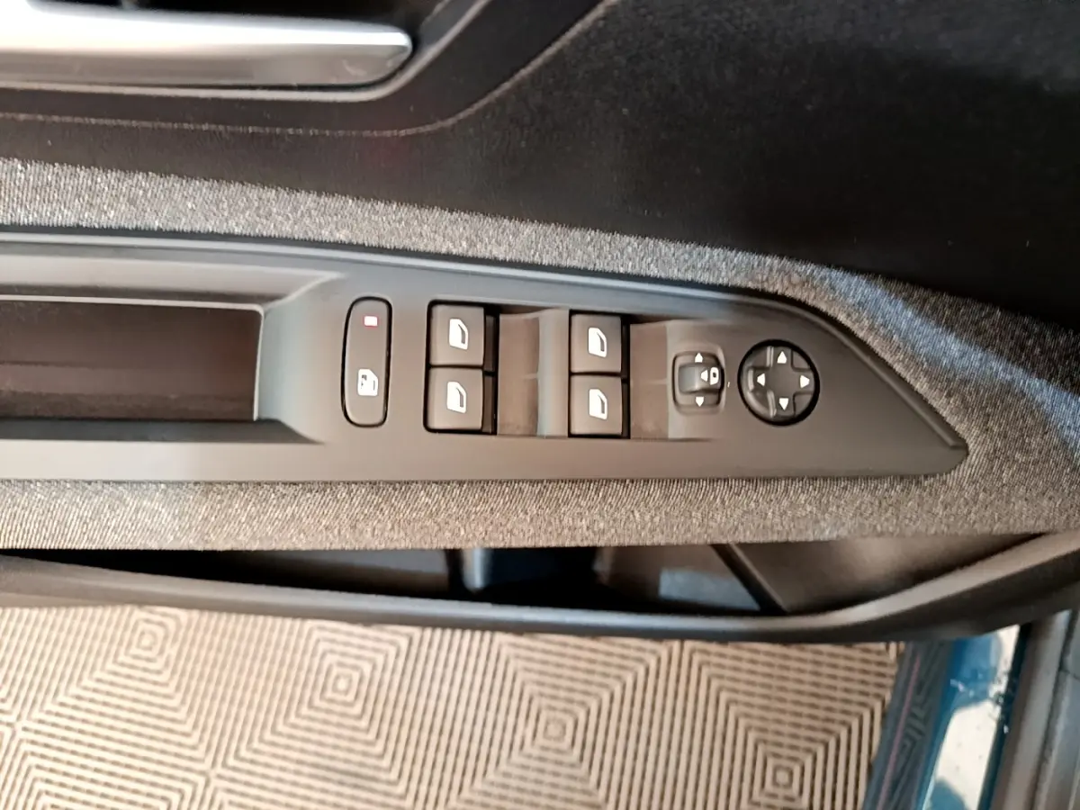 Vue rapprochée des commandes de lève-vitres et rétroviseurs sur la porte côté conducteur d’un Peugeot 3008 bleu.