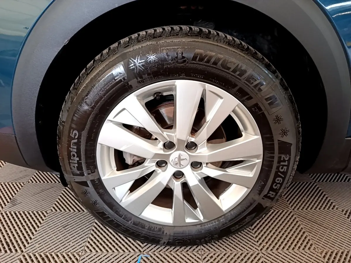 Gros plan sur la roue avant gauche d’un Peugeot 3008 bleu, mettant en valeur la jante argentée et le pneu Michelin Alpine 5.