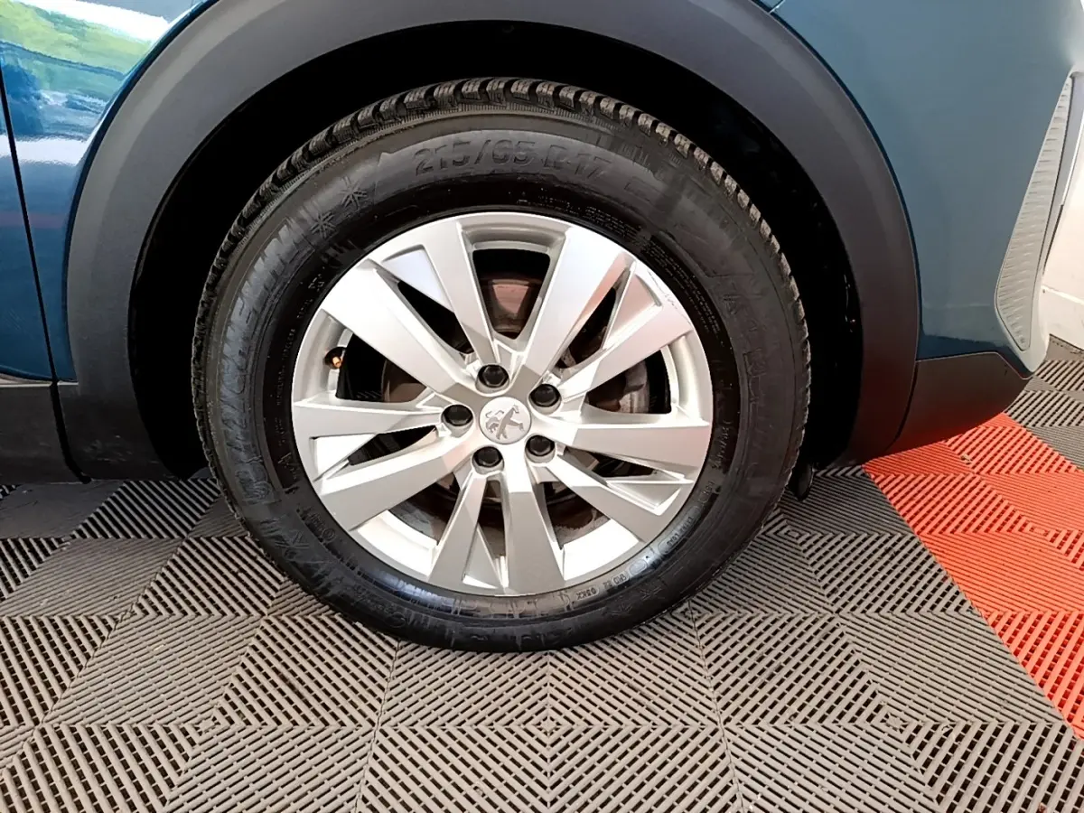 Gros plan sur la roue avant gauche d’un Peugeot 3008 bleu 2022 avec jante alliage argentée et logo lion central.