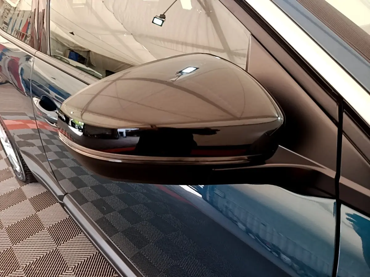 Gros plan sur le rétroviseur noir côté gauche d’un Peugeot 3008 bleu, reflet de l’environnement intérieur visible.