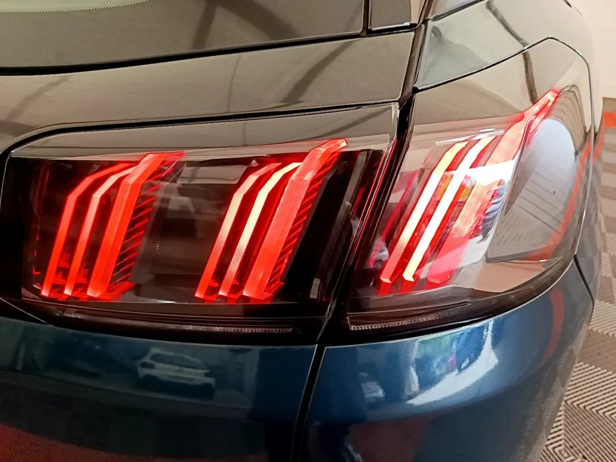 Gros plan sur le feu arrière droit rouge d’un Peugeot 3008 bleu, soulignant la carrosserie brillante et les lignes modernes.