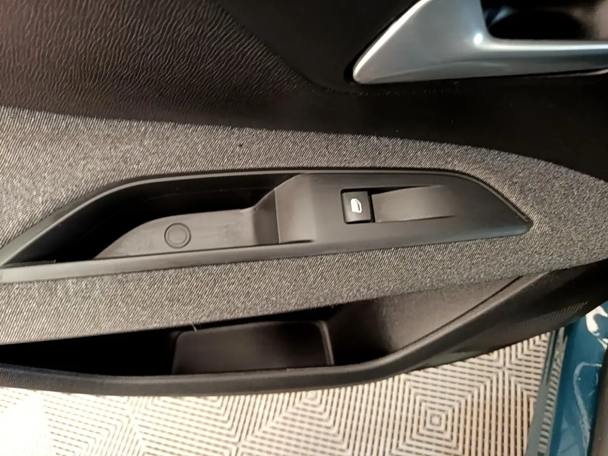 Détail de la commande de lève-vitre côté conducteur sur porte intérieure tissu noir du Peugeot 3008 bleu 2022.