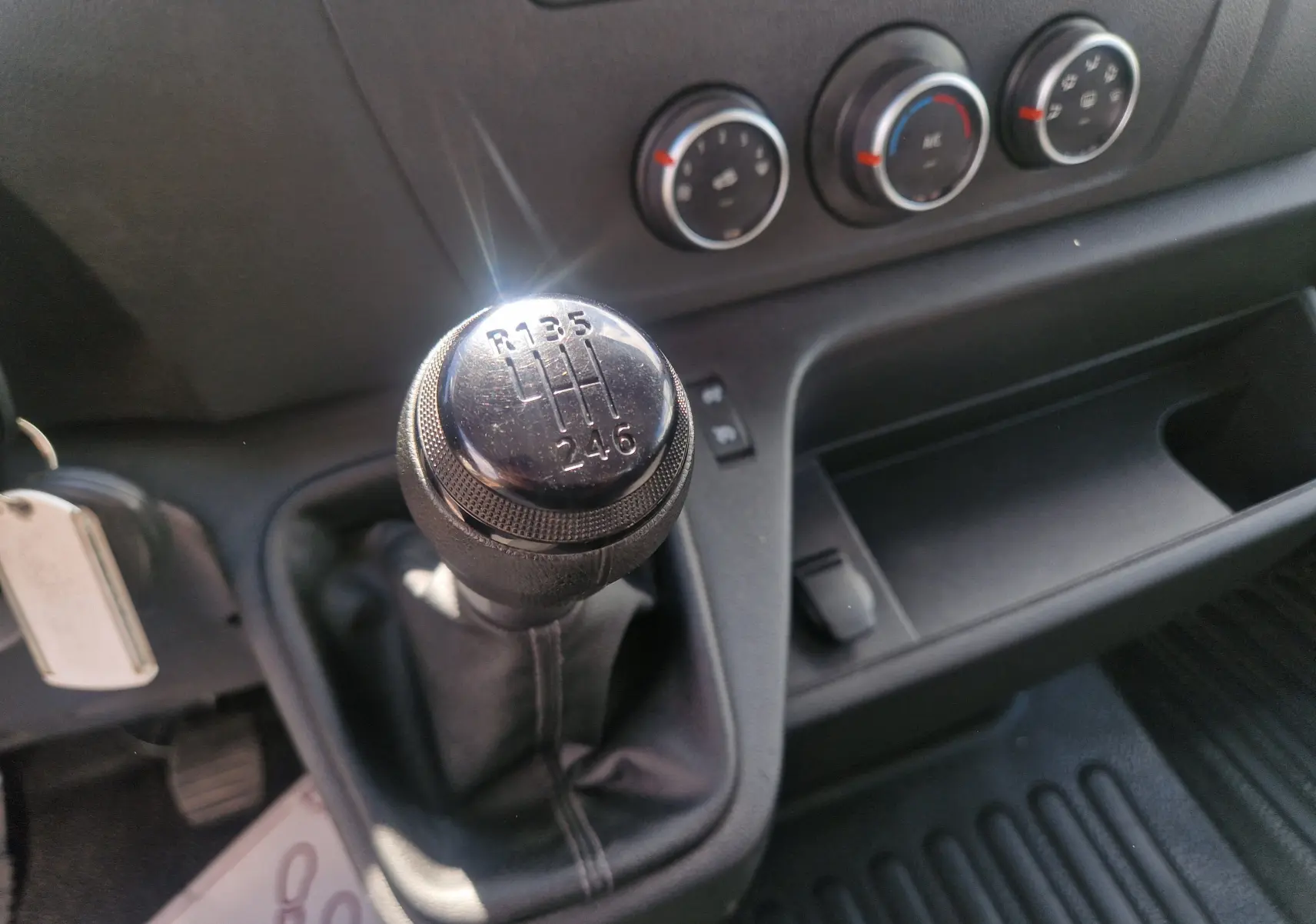 Gros plan sur le levier de vitesses manuel noir du Renault Master Châssis Cabine blanc, avec commandes de climatisation en arrière-plan.