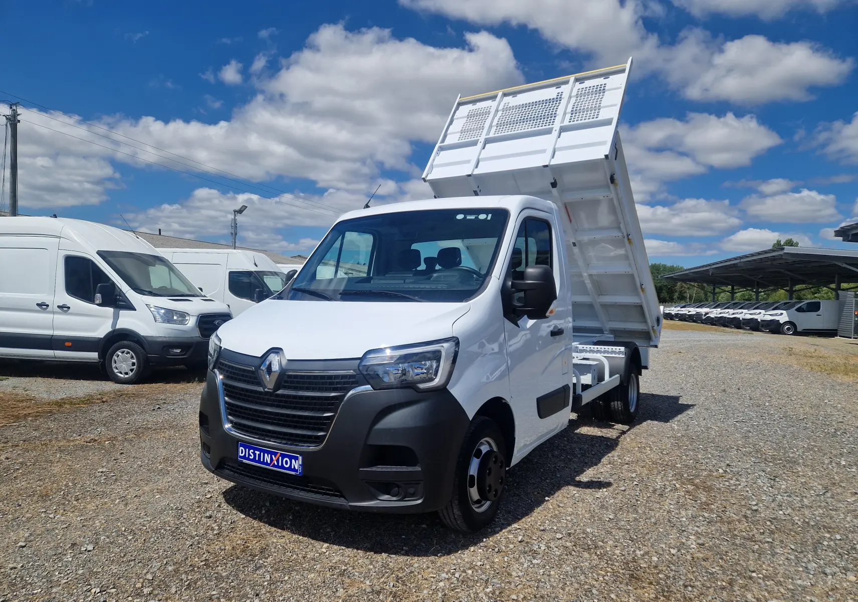 Renault Master Benne blanc en 3/4 avant droit avec benne relevée et roues jumelées sur terrain extérieur.