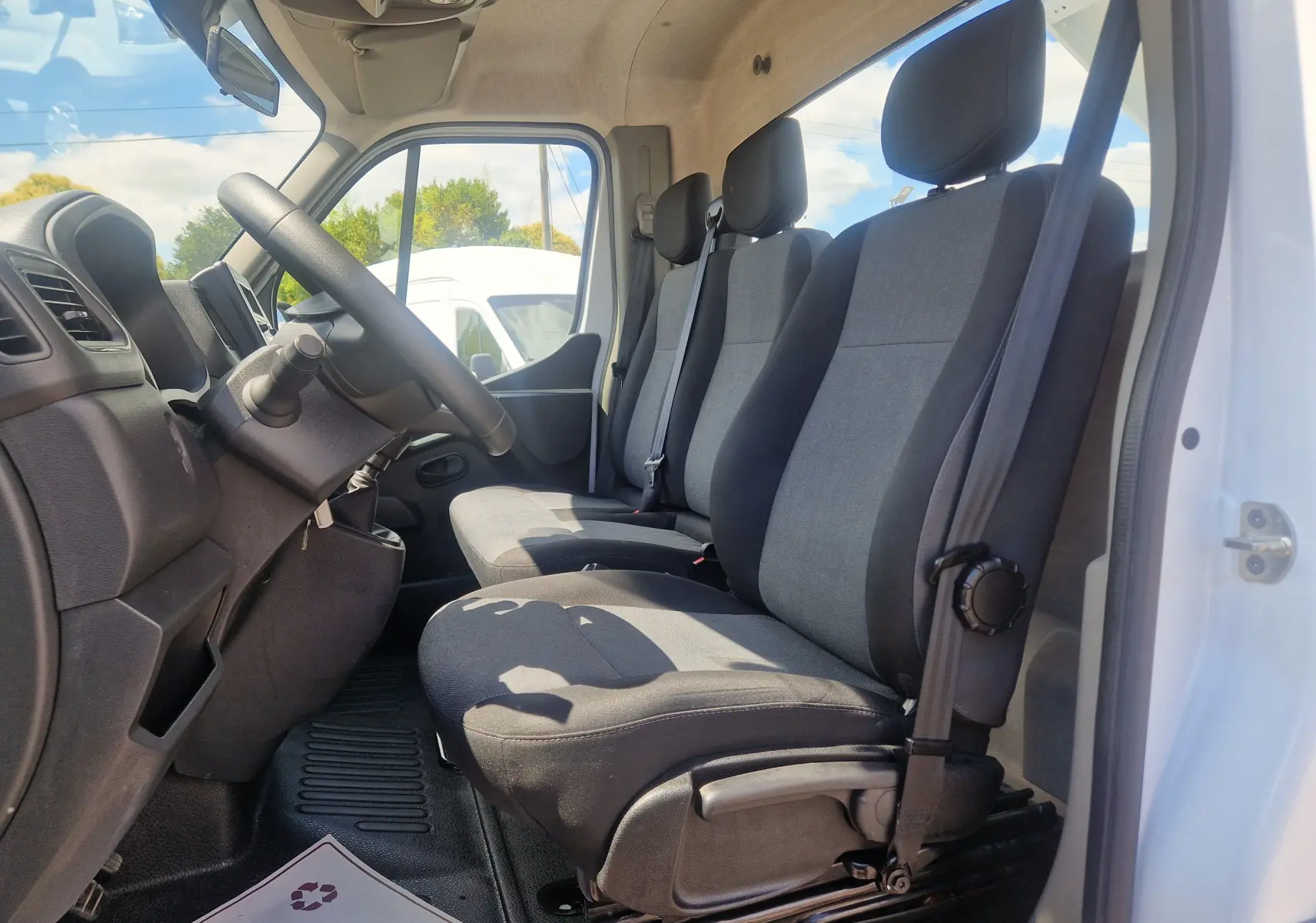 Vue intérieure côté conducteur du Renault Master Châssis Cabine blanc 2024, montrant les sièges tissu gris et noir, volant et tableau de bord.