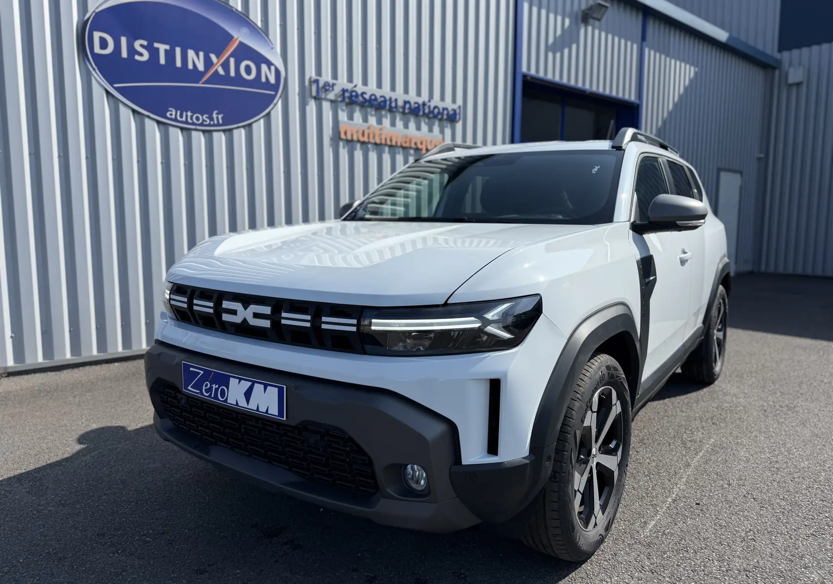 Vue 3/4 avant droit du Dacia Duster Hybrid 155 Journey blanc glacier avec calandre noire et jantes noires.