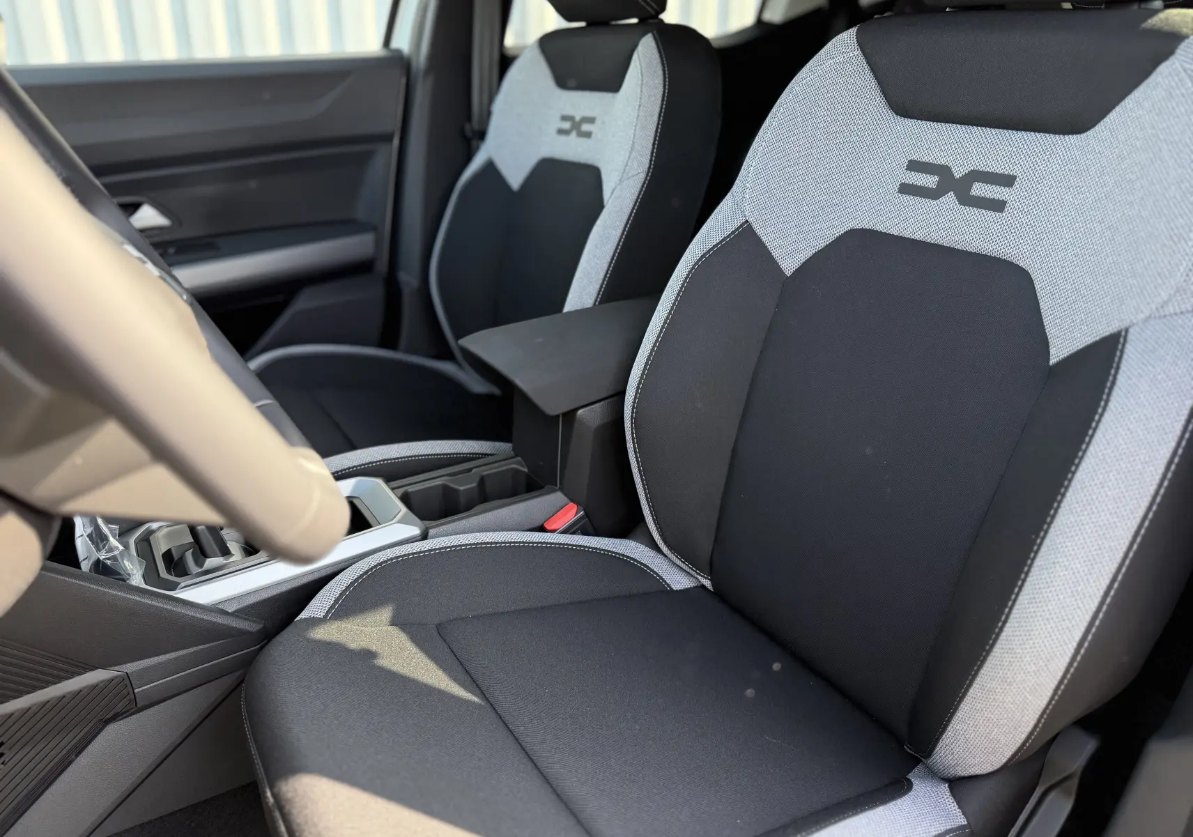 Vue intérieure rapprochée des sièges avant gris clair et noir du Dacia Duster Hybrid 155 Journey avec logo distinctif brodé.