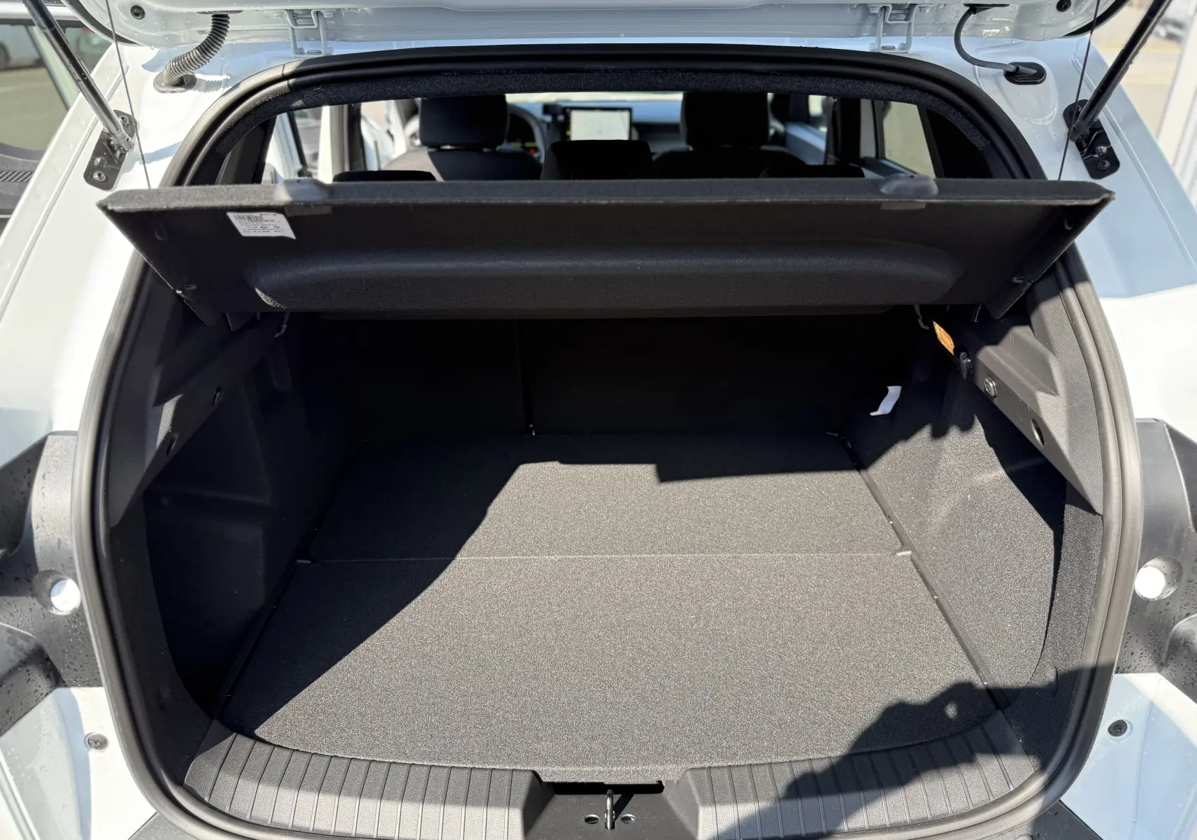 Coffre ouvert vu de l'arrière d'un Dacia Duster Hybrid 155 Journey blanc glacier, montrant un espace de chargement vide.