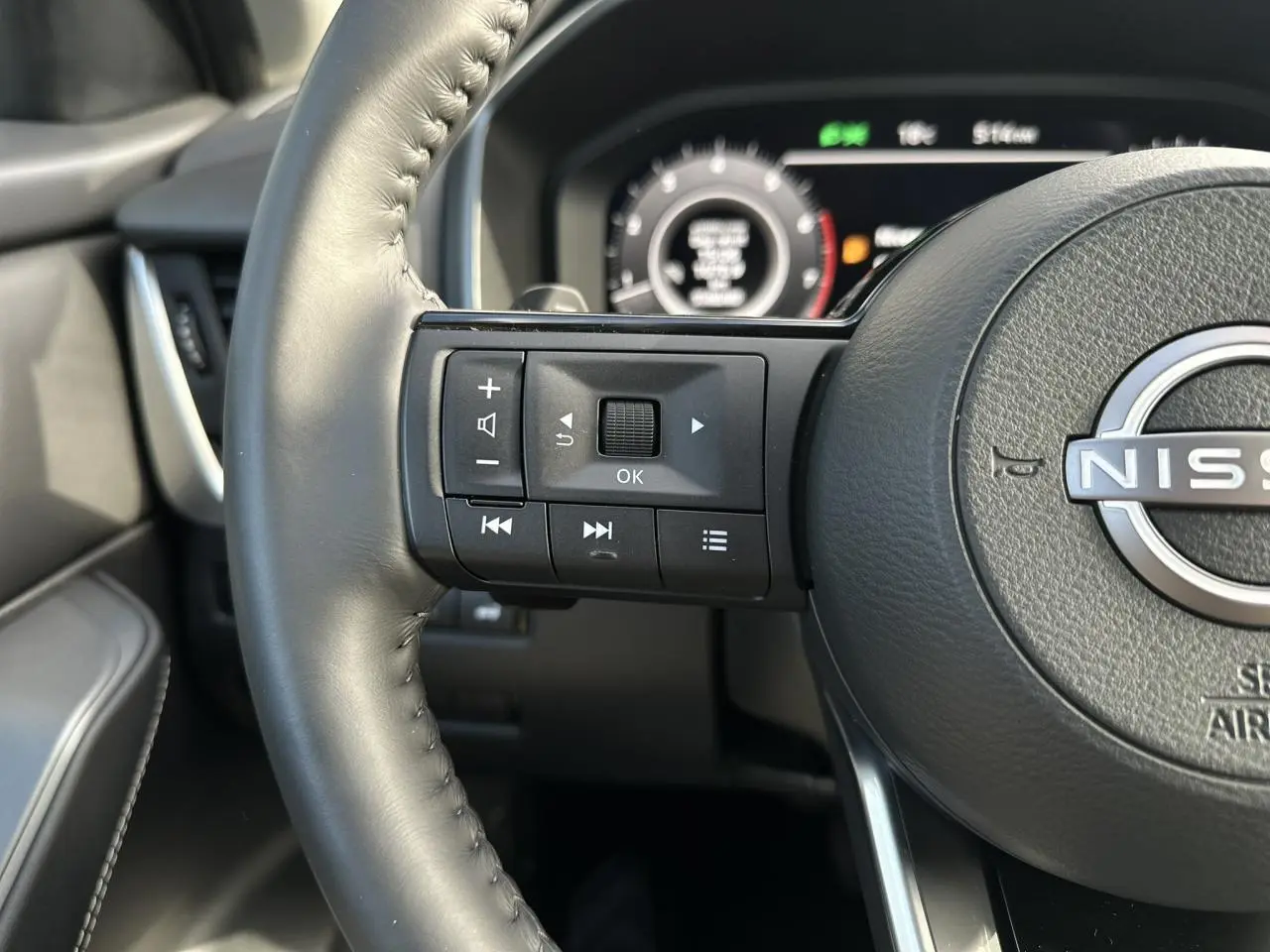 Gros plan sur le volant cuir noir du Nissan Qashqai 2025 avec commandes intégrées et tableau de bord numérique flou.
