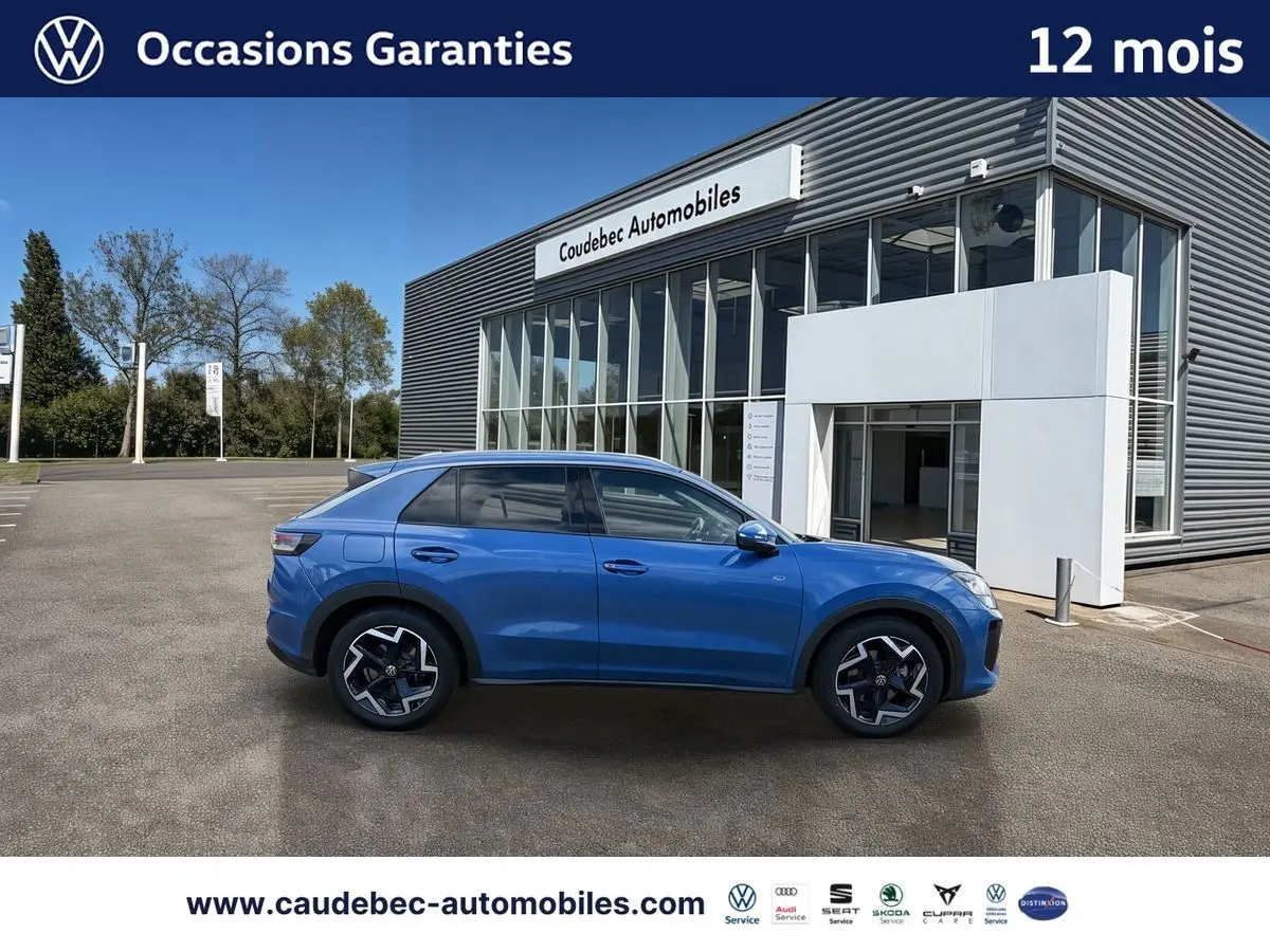 Vue de profil côté gauche d'un Volkswagen T-Roc bleu métallisé garé devant un bâtiment moderne.