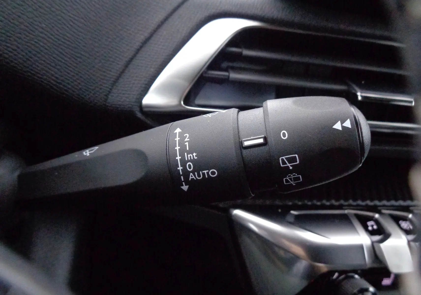 Gros plan sur la manette d'essuie-glace du Peugeot 3008 gris Artense, avec commandes et aérateurs en arrière-plan.